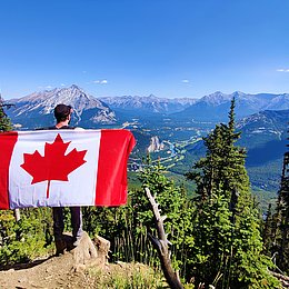 Junger Mann mit kanadischer Flagge blickt auf Berge © Maxime Doré / unsplasch.com